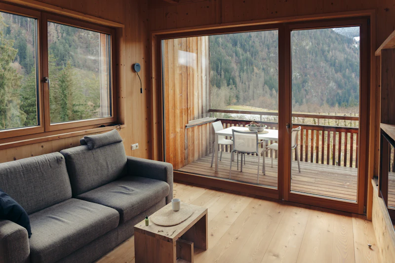 Wohnzimmer mit Sofa und grosser Glastür zum Holzbalkon