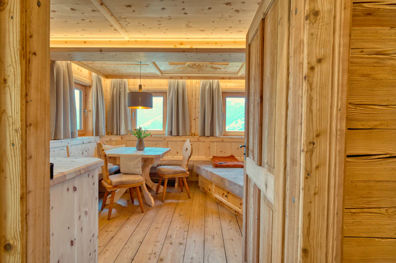 Stube mit Esstisch, Eckbank und Wänden aus hellem Holz